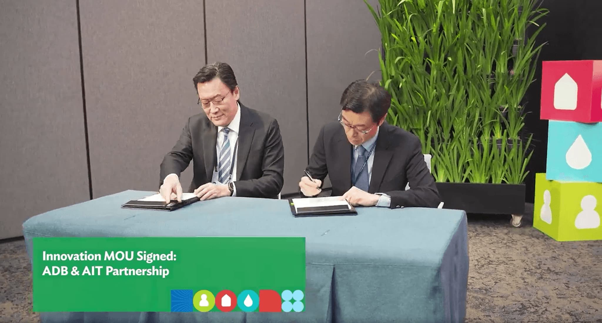 "Two business professionals signing an MOU for the ADB and AIT partnership, with greenery in the background."