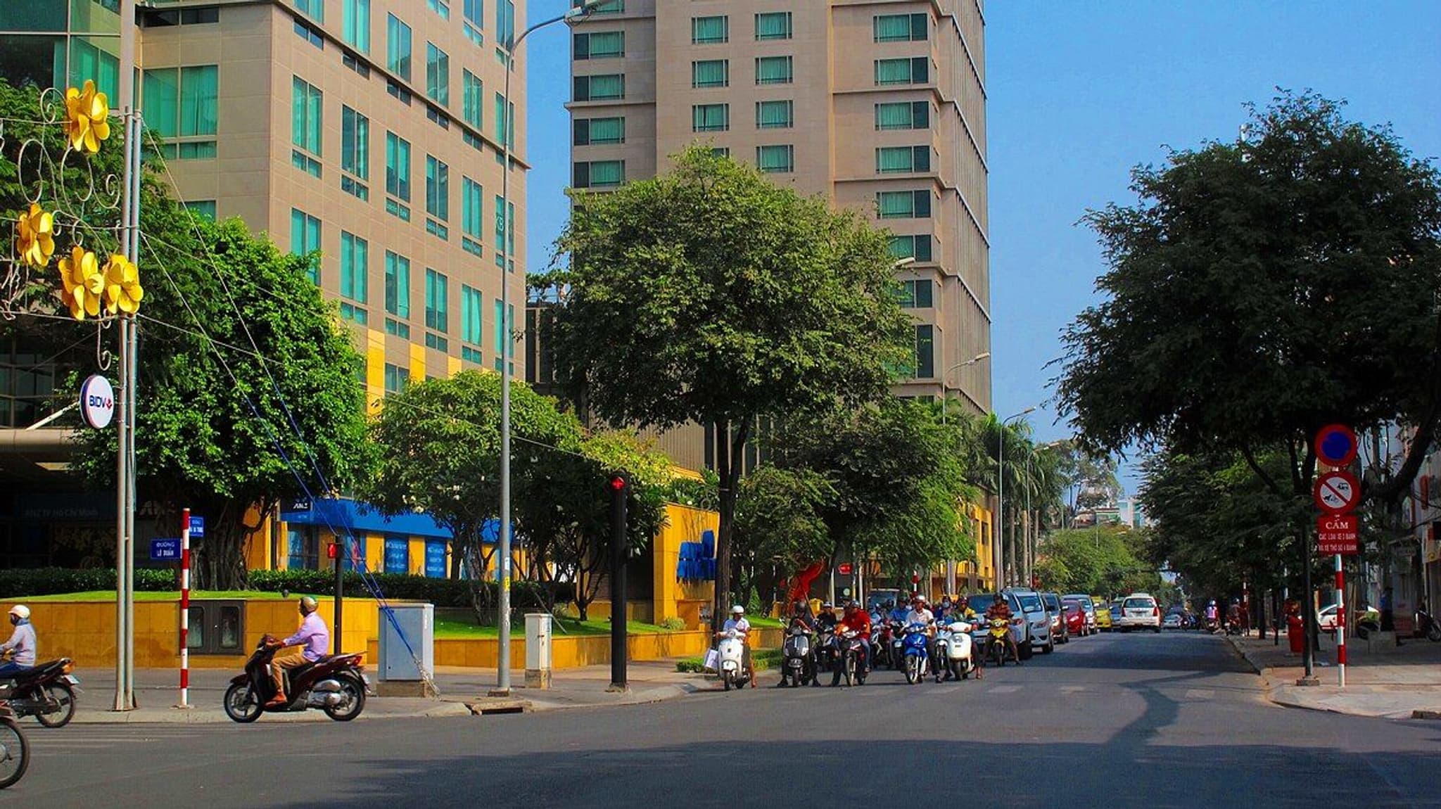 Bustling street in Saigon, showcasing modern buildings, greenery, and motorbikes on a sunny day.