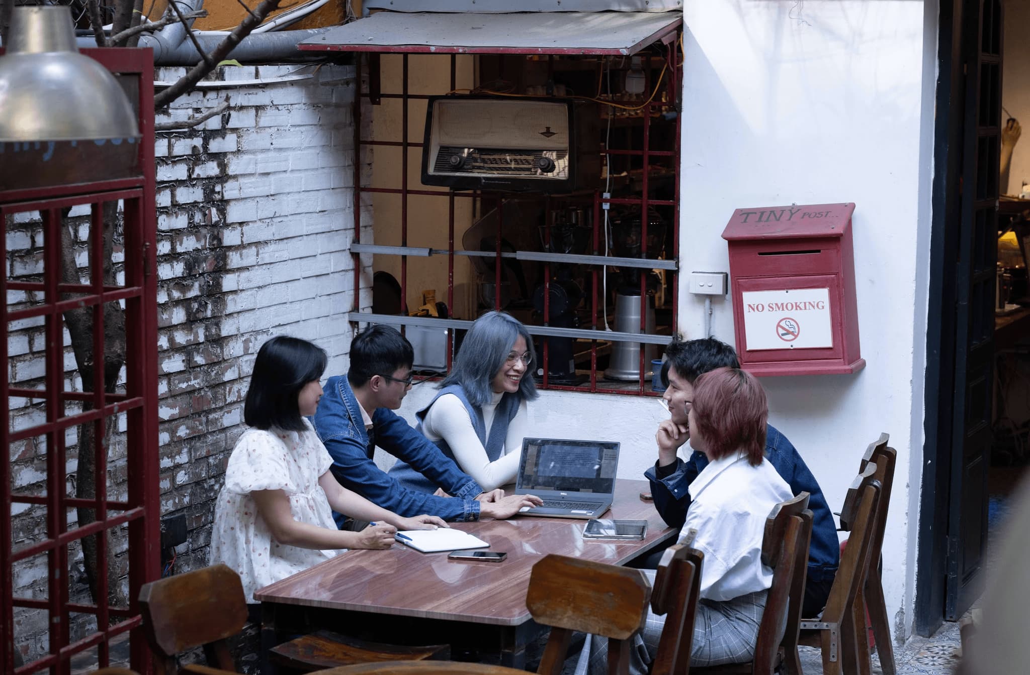 Group of six colleagues collaborating at an outdoor café, engaged in discussion around a laptop.