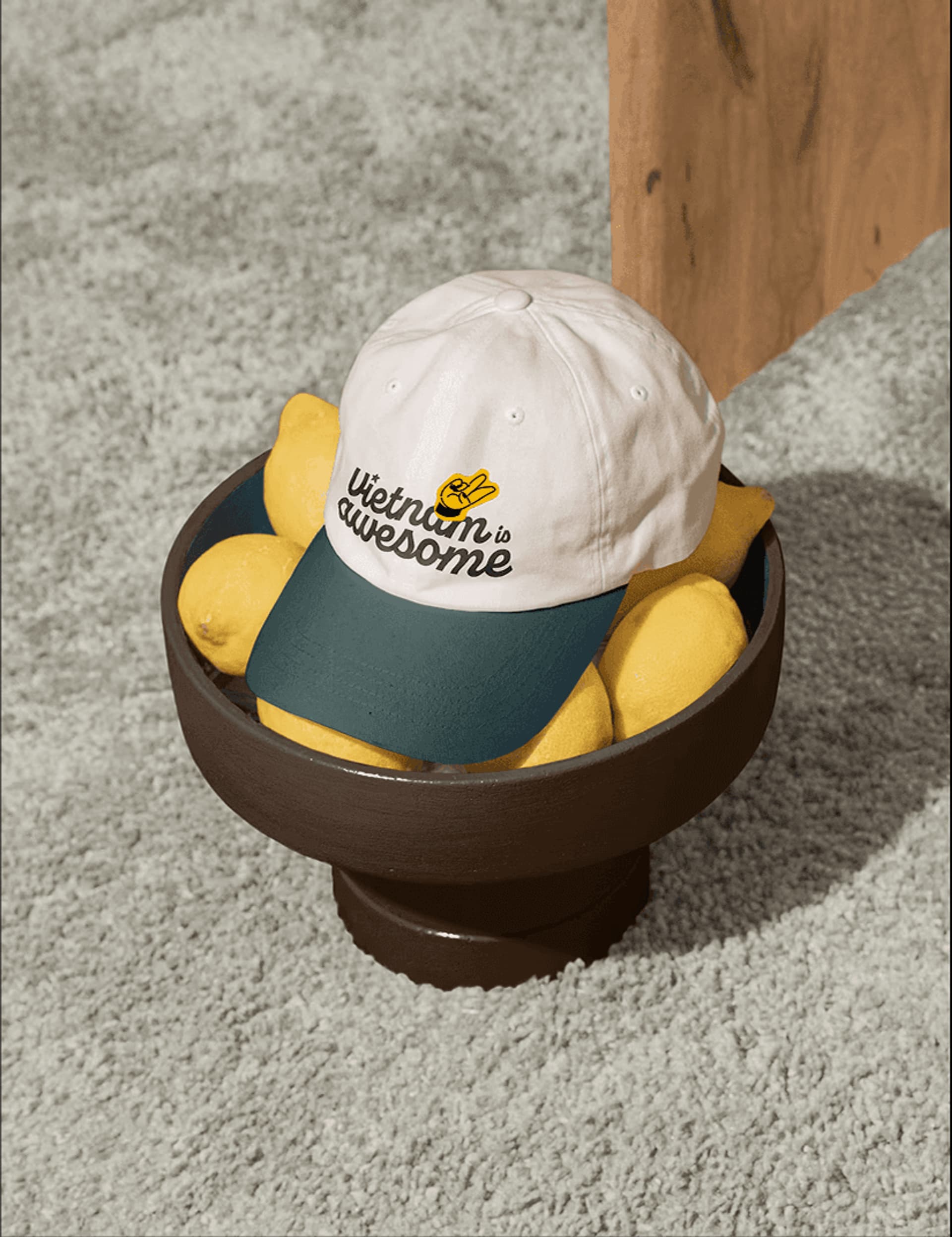 White and green cap with "Vietnam is awesome" text resting on a bowl of lemons on a textured surface.